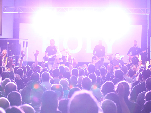 Bright pink sweeping lights cover a congregation of men worshipping