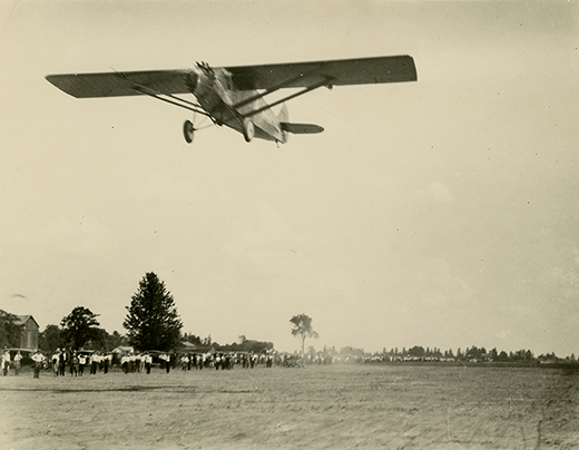 An old photo of a plane flying above a field